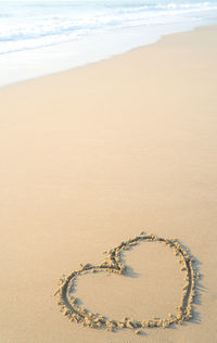 Hand drawing a heart shape on sandy beach