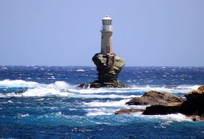 Lighthouse on rock by sea against clear sky