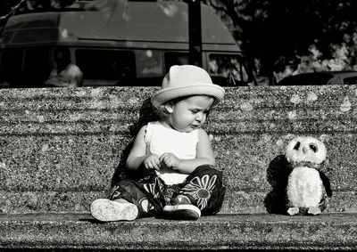 Baby girl sitting by owl toy on bench during sunny day