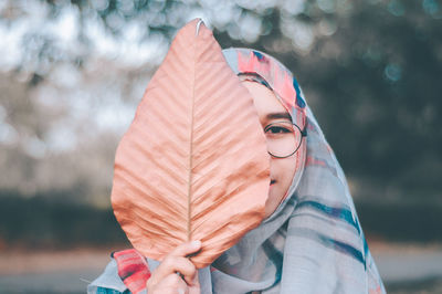 Close-up portrait of teenage girl covering face with dry leaf