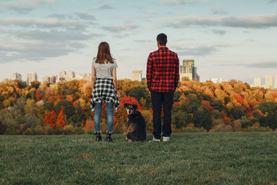 Rear view of people with dog standing on grass against sky