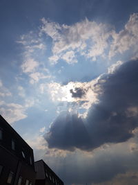 Low angle view of sunlight streaming through buildings against cloudy sky