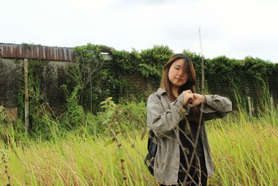 Young woman standing by tree against sky