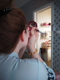 Rear view of woman applying make-up at home