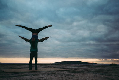 Full length of man balancing woman on hand by sea against cloudy sky