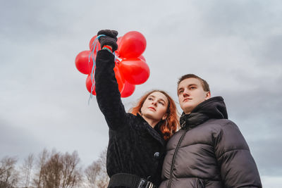 Low angle view of couple with balloons standing against sky