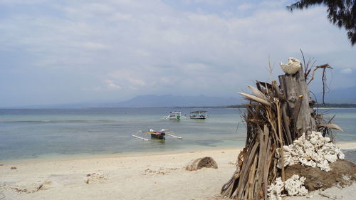 Outrigger canoe moored at beach against cloudy sky on sunny day