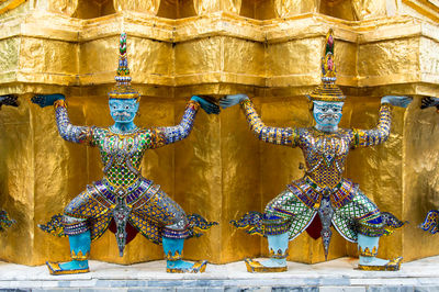 Close-up of demon statue against gold wall at wat phra kaew