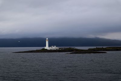 Lighthouse amidst sea and buildings against sky