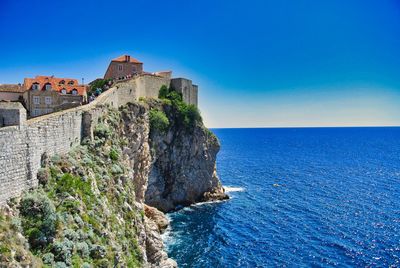 Buildings by sea against clear blue sky