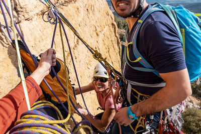 Friends climbing mountain with rope and safety harness
