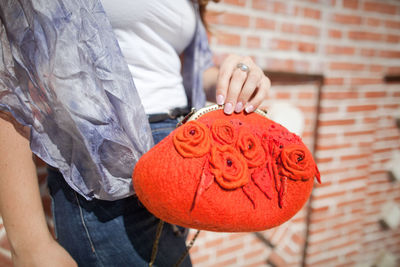 Midsection of woman holding red standing against brick wall