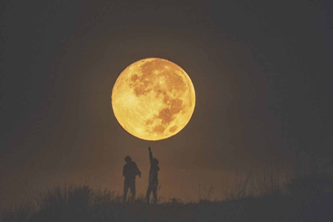 FULL LENGTH OF MAN STANDING ON FIELD AGAINST MOON