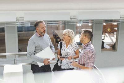 Businesspeople discussing by railing in modern office