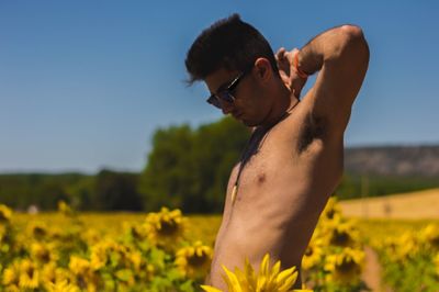 Shirtless man standing on field against clear sky
