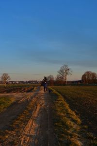 Rear view of person cycling on field against sky