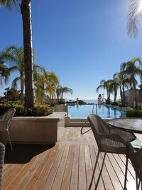 Empty chairs by swimming pool against clear sky