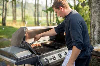 Side view of man preparing food on barbecue grill