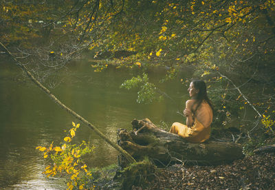 Woman in yellow dress sitting on a log on the shore of a lake, slovenia