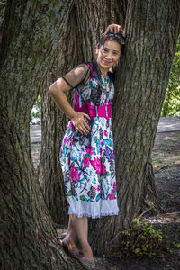 Portrait of a smiling young woman standing on tree trunk