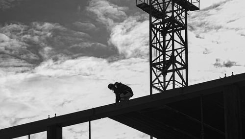 Low angle view of crane and worker on building structure against sky