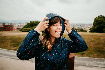 Smiling young woman with raincoat against field