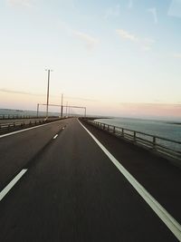 Road by sea against sky during sunset