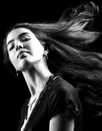 Side view portrait of young woman tossing hair against black background