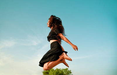 Low angle view of woman jumping against blue sky