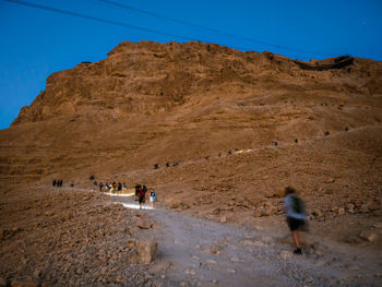 People walking on arid landscape against clear sky