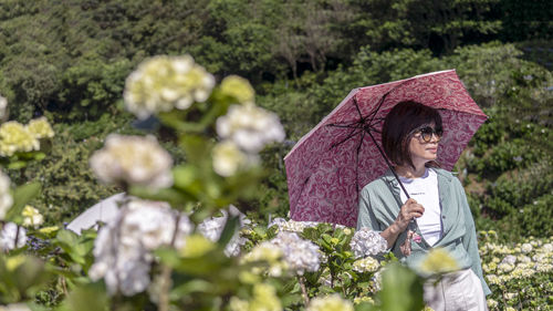 Woman holding umbrella while standing by plants during rainy season