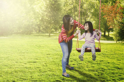 Happy mother pushing daughter sitting on swing in playground