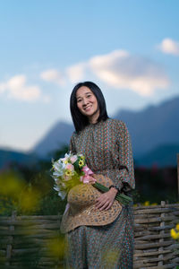 Happy woman holding umbrella standing on rock against sky