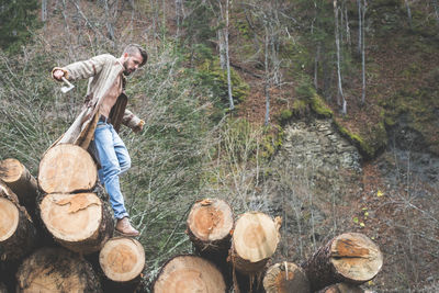 Young man walking on logs of wood in forest 