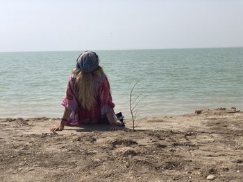 Rear view of woman standing at beach against clear sky