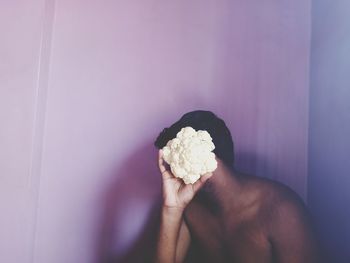 Shirtless man holding vegetable sitting by wall