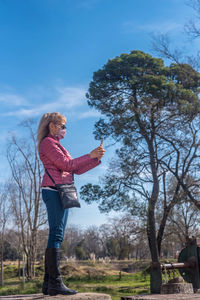 Full side view of an adult woman with face mask and sunglasses standing taking a picture