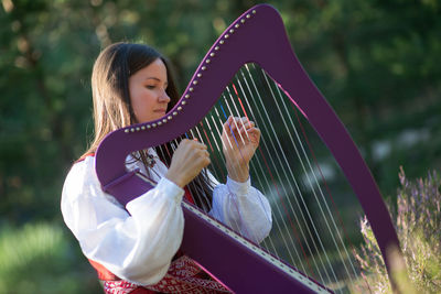 Woman playing harp against trees in forest