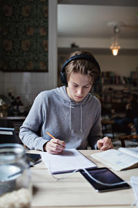 Studious teenage boy listening music while studying on table at home