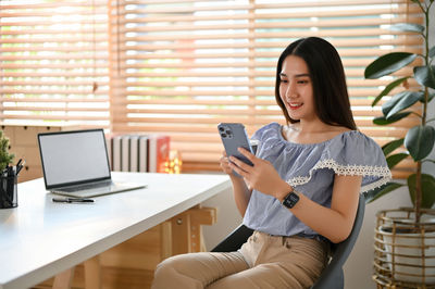 Young woman using mobile phone while sitting on table