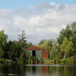 House and trees by lake against sky
