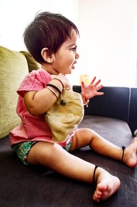 Side view of baby girl sitting on sofa at home