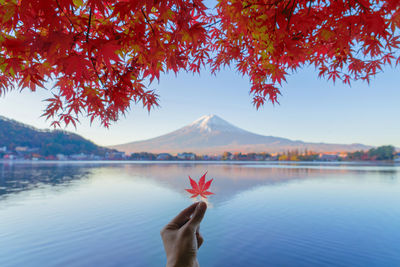 Person hand by lake against sky