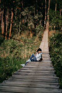 Man photographing while sitting on rope bridge