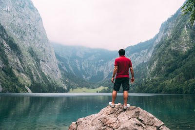 Rear view of man standing on rock by lake