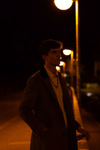 Young woman looking away while standing on street at night