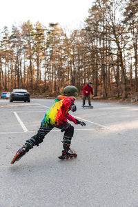 Back view of active anonymous kid in helmet rollerblading on parking in autumn park and having fun