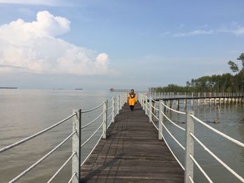 Woman walking on footbridge over lake against sky