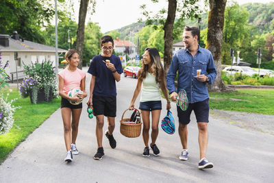 Happy multiracial family with picnic supplies walking on road