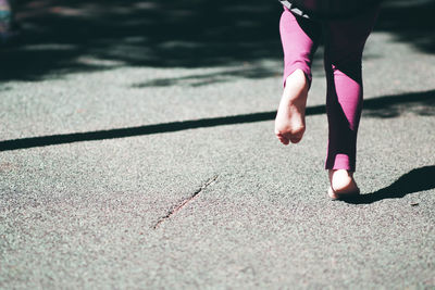 Low section of woman walking on road during sunny day